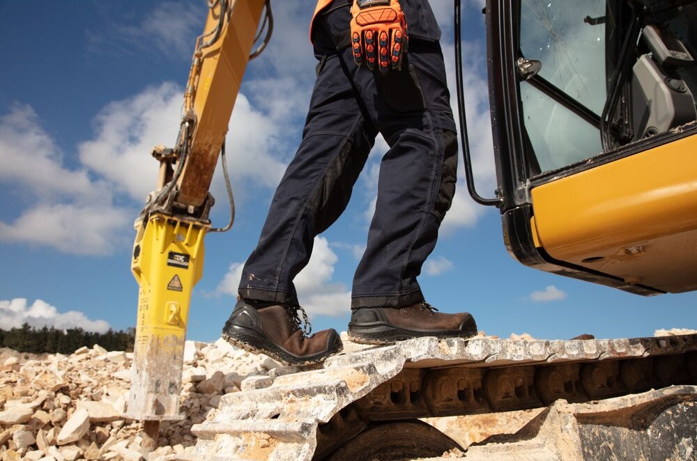 Detalhe de calçado e luvas de segurança junto a maquinaria pesada